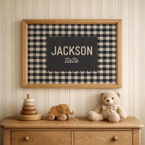 May include: A rectangular wooden frame containing a black and white gingham fabric background. Centered on the fabric is a dark gray scalloped-edge plaque featuring the text JACKSON in a bold sans-serif font and tate in a cursive script.