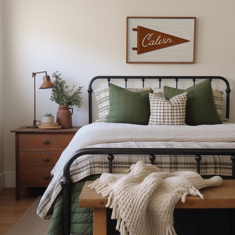 May include: A bedroom featuring a black metal bed frame with a white and gray plaid comforter, two solid olive green pillows, and a plaid accent pillow. A wooden bench with a cream-colored knit throw blanket sits at the foot of the bed.