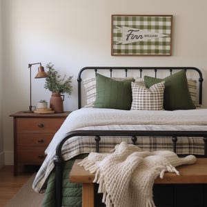 May include: A framed wall sign featuring a green and white buffalo check pattern with a white pennant overlay displaying the name Finn William in black script. The sign is positioned above a black metal bed frame with green and plaid pillows.