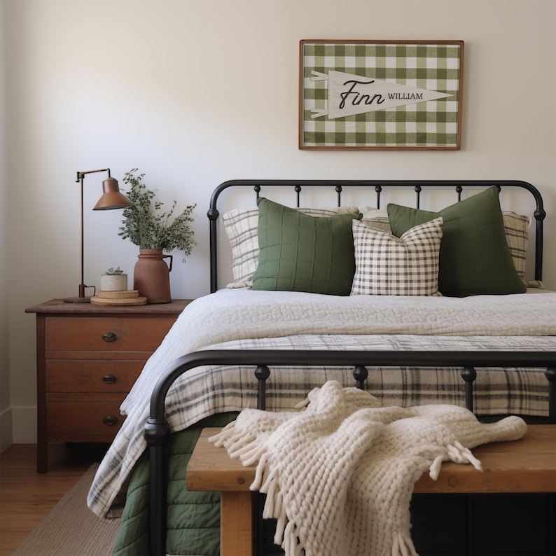 May include: A framed wall sign featuring a green and white buffalo check pattern with a white pennant overlay displaying the name Finn William in black script. The sign is positioned above a black metal bed frame with green and plaid pillows.