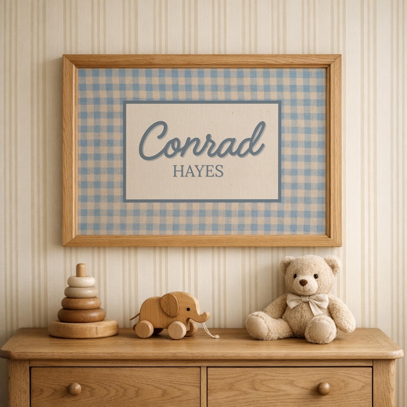 May include: A rectangular wooden frame containing a print with a light blue and white gingham pattern background. A central white rectangle features the name Conrad in a blue script font above the name HAYES in a blue block font.