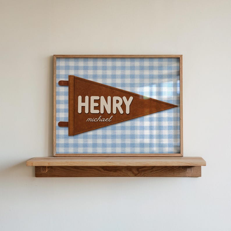 May include: Framed pennant with the name "HENRY" in white block letters and the name "michael" in a smaller font. The pennant is brown and set against a blue and white gingham background. The frame is a light brown color.