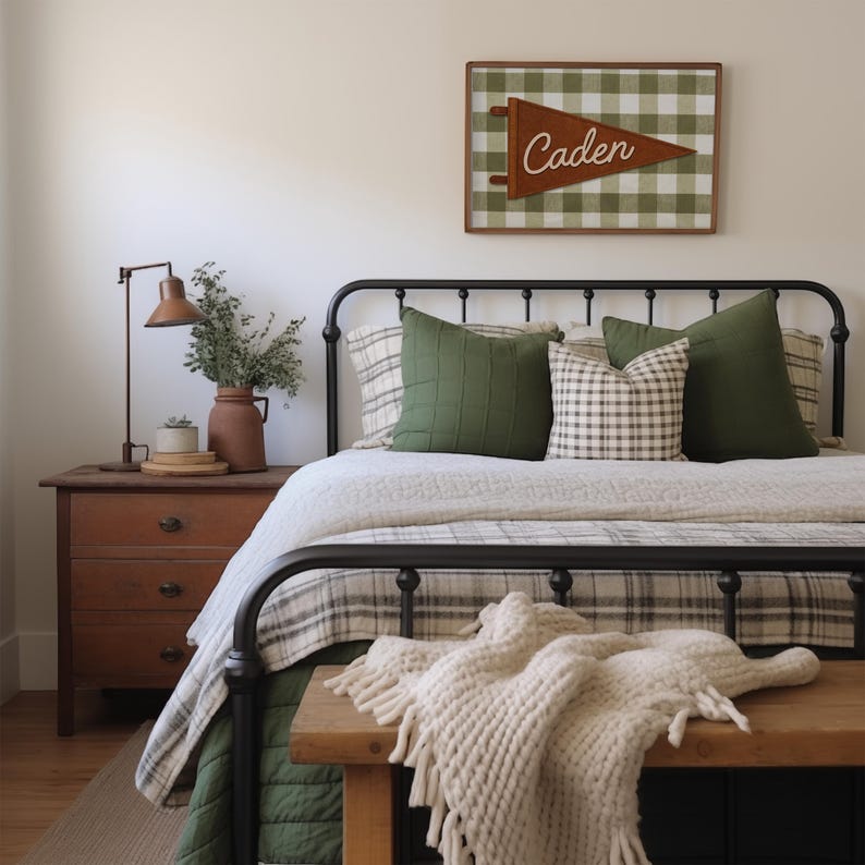 May include: A bedroom scene featuring a black metal bed frame with a green and white plaid patterned blanket and pillows. A wooden bench with a cream-colored knitted throw is at the foot of the bed. A wooden sign with the name "Caden" hangs above the bed.
