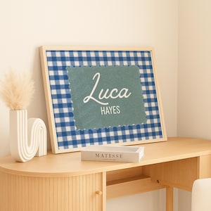 May include: A framed rectangular print featuring a blue and white gingham pattern background with a centered sage green scalloped patch. The patch displays the name Luca in a white script font above the name HAYES in a white sans-serif font.
