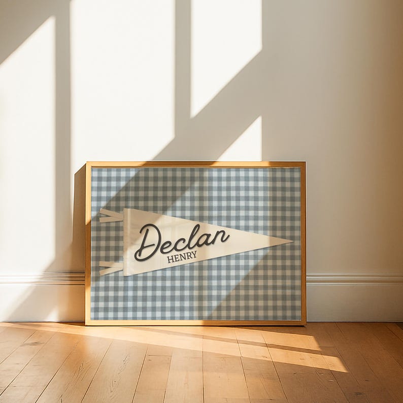 May include: A rectangular framed print featuring a light cream-colored triangular pennant centered on a blue and white gingham checkered background. The pennant displays the name Declan in a large script font with Henry in a smaller sans-serif font.