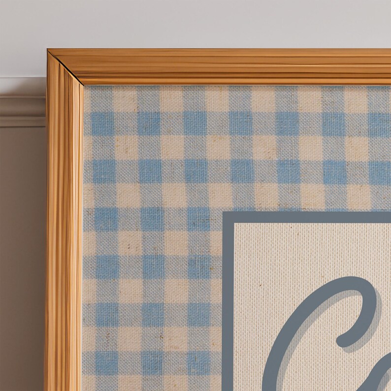 May include: A framed wall art piece featuring a light blue and cream gingham pattern background. A central rectangular panel with a cream-colored surface is bordered by a dark gray line. The frame is made of light-toned wood with a smooth finish.