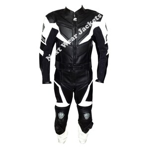 Peut inclure: Combinaison de course de moto noire et blanche. La combinaison présente une base en cuir noir avec des accents blancs sur les épaules, les bras, la poitrine et les jambes. Le texte "Next Wear Jackets" est visible sur la poitrine. La combinaison comprend une ceinture et des genouillères.