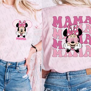 May include: Pink t-shirt featuring a Minnie Mouse graphic with a pink bow and the word "MAMA". The back of the shirt has a repeating "MAMA" design with Minnie Mouse wearing heart-shaped sunglasses.