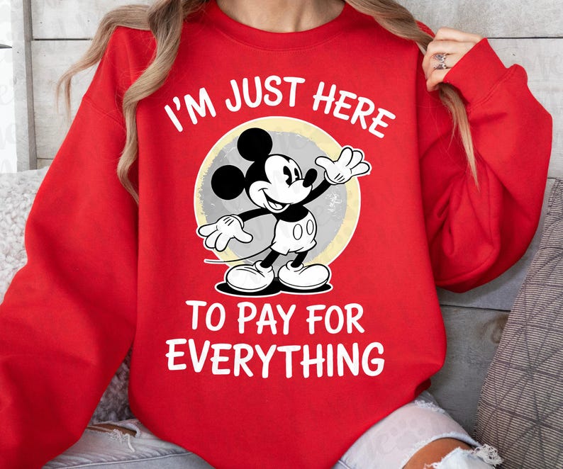 May include: Red sweatshirt featuring Mickey Mouse with the text "I'M JUST HERE TO PAY FOR EVERYTHING." Mickey Mouse is in black, white, and gray, set against a yellow and gray circle.