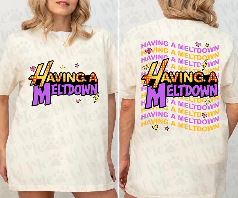 Puede incluir: Camiseta color crema con el texto "HAVING A MELTDOWN" en amarillo y morado, con un rayo y una estrella. La parte trasera de la camiseta repite la frase con gr&aacute;ficos adicionales.