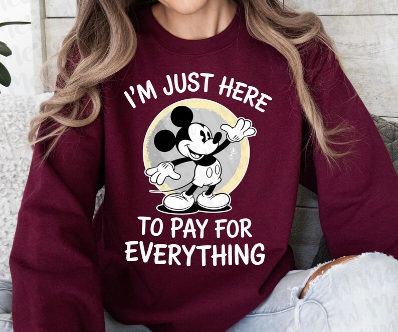 May include: Burgundy sweatshirt featuring Mickey Mouse with the text "I'M JUST HERE TO PAY FOR EVERYTHING." Mickey Mouse is in black, white, and gray, standing in front of a yellow and gray circle.