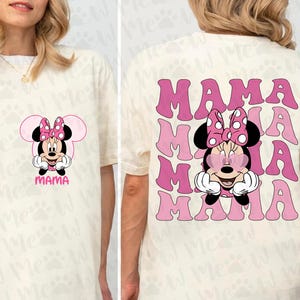 May include: Cream-colored t-shirt featuring a Minnie Mouse graphic with a pink bow and the word "MAMA". The back of the shirt displays the word "MAMA" repeated in pink, with a Minnie Mouse graphic.