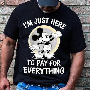 May include: Black t-shirt featuring Mickey Mouse with the text "I'M JUST HERE TO PAY FOR EVERYTHING". The graphic shows Mickey Mouse in a classic pose against a yellow and gray background.