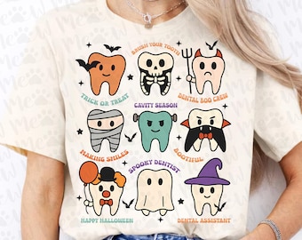 Op de afbeelding: Crèmekleurig T-shirt met cartoon tanden met Halloween thema's. Ontwerpen zijn onder meer een vleermuis, skelet, mummie, vampier, spook en clown. Tekst bevat "Trick or Treat", "Cavity Season" en "Happy Halloween."