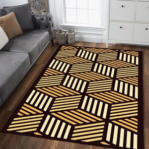 May include: A rectangular area rug with a geometric pattern. The rug features a repeating design of angled, parallel lines in shades of beige and cream against a dark brown background. The rug is placed on a wooden floor.
