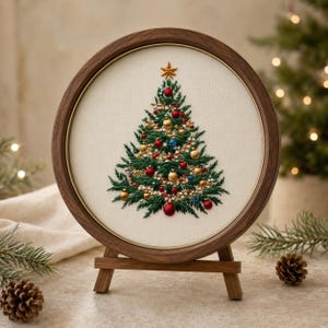 May include: A circular wooden embroidery hoop frame containing a hand-stitched Christmas tree on off-white fabric. The tree features dark green thread branches decorated with small red, gold, and blue spherical ornaments and a gold star topper.