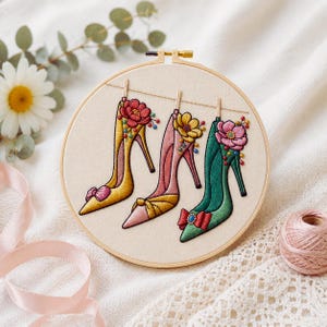 Könnte beinhalten: Gesticktes Hoop-Art mit drei hochhackigen Schuhen in Gelb, Rosa und Grün. Jeder Schuh ist mit floralen Verzierungen und Schleifen versehen. Das Kunstwerk ist vor einem neutralen Hintergrund platziert, mit einer Gänseblümchen und einem Band.