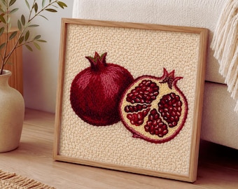 May include: A framed artwork featuring a detailed embroidered pomegranate design. One whole pomegranate and one cut in half, revealing the seeds, are depicted in shades of red and burgundy against a beige background. The frame is made of light-colored wood.