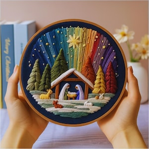 Può includere: Scena natalizia ricamata in un cerchio di legno rotondo. L'opera raffigura una scena della natività con un cielo color arcobaleno, alberi e animali. Il cerchio è tenuto da due mani.