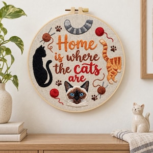 May include: A circular embroidery hoop featuring the text Home is where the cats are stitched in orange and red thread. The design includes a black cat silhouette, an orange tabby cat, a Siamese cat face, yarn balls, and paw prints on linen.