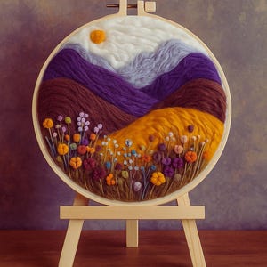 Op de afbeelding: Een landschapsscène van vezelkunst in een houten borduurring. Het kunstwerk toont een bergketen in tinten paars, bruin en wit, met een gele zon. De voorgrond heeft kleurrijke bloemen en een gouden veld. De ring wordt op een kleine houten ezel getoond.