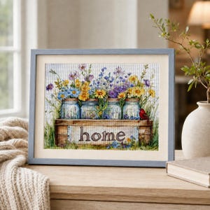 May include: A framed cross-stitch artwork featuring four glass mason jars filled with colourful wildflowers, including yellow, blue, and purple blossoms. The jars sit inside a wooden crate with the word home printed in brown lowercase letters.