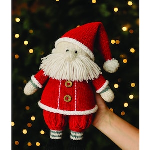 May include: A knitted Santa Claus doll in a red suit with a white beard and hat. The doll has black boots and is holding a gift. The words "Merry Christmas" are written at the top.