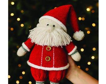 May include: A handmade knitted Santa Claus doll in a red suit with a white beard and hat. The doll has black boots and is holding a gift. The words "Merry Christmas" are written at the top.