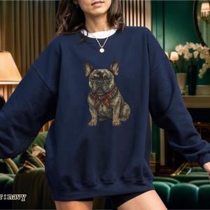 May include: Navy blue sweatshirt featuring a detailed illustration of a French Bulldog wearing a red and green plaid scarf. The dog is centered on the front of the sweatshirt. The text "color: navy" is at the bottom left of the image.