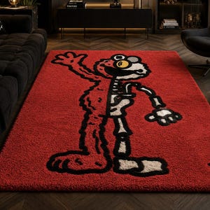 Puede incluir: Una alfombra rectangular roja con un dise&ntilde;o de personaje de dibujos animados. El dise&ntilde;o est&aacute; dividido, mostrando el exterior del personaje a la izquierda y un esqueleto a la derecha. El personaje tiene contornos negros, ojos amarillos y un esqueleto beige. La alfombra es de material suave y afelpado.