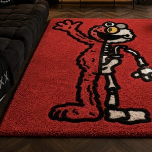 Puede incluir: Una alfombra rectangular roja con un dise&ntilde;o de personaje de dibujos animados. El dise&ntilde;o es una versi&oacute;n esquel&eacute;tica de un personaje con contornos negros y huesos blancos. La alfombra tiene una textura afelpada y est&aacute; colocada sobre un suelo de madera oscura.