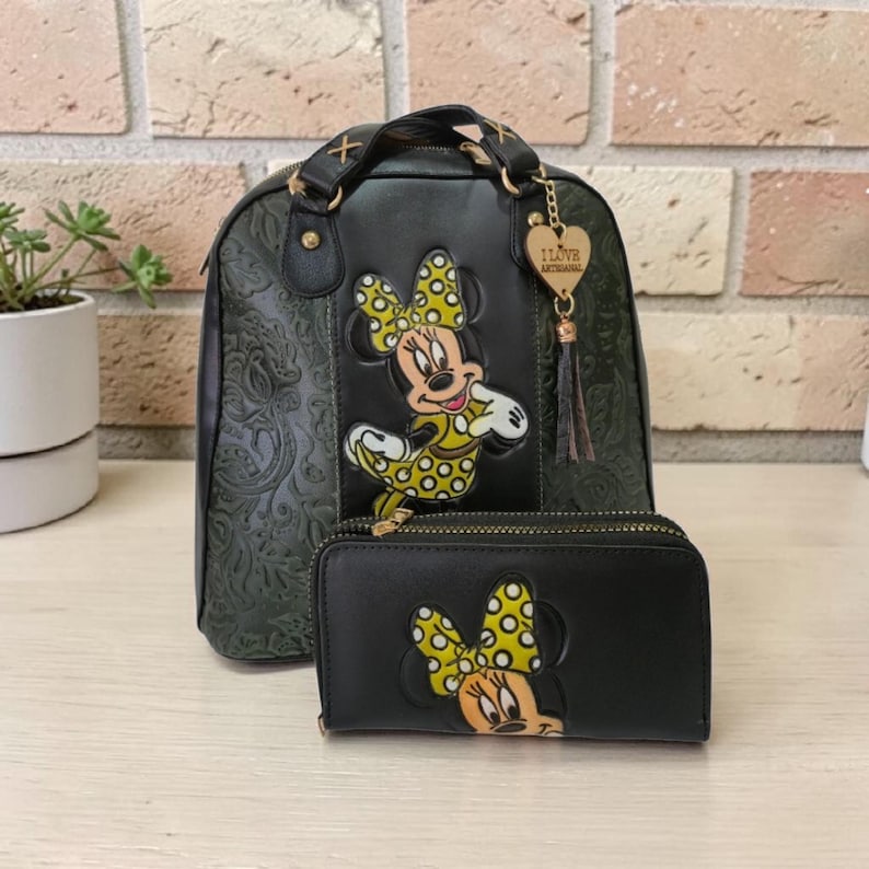 Op de afbeelding: Zwarte rugzak- en portemonneeset met Minnie Mouse. De rugzak heeft een bloemreli&euml;f en goudkleurige hardware. De portemonnee en rugzak hebben beide een Minnie Mouse applicatie met een gele stippen strik.