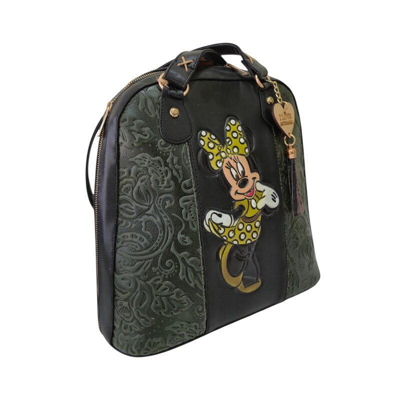 Op de afbeelding: Zwarte en groene handtas met een Minnie Mouse-ontwerp. De tas heeft een bloemreli&euml;fpatroon aan de zijkant en een goudkleurige ritssluiting. Een goudkleurige bedel met een kwastje hangt aan de handgreep.