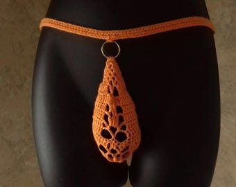 May include: Orange crochet thong with a decorative openwork design. The thong features a ring detail and a waistband. The garment is displayed on a black mannequin.