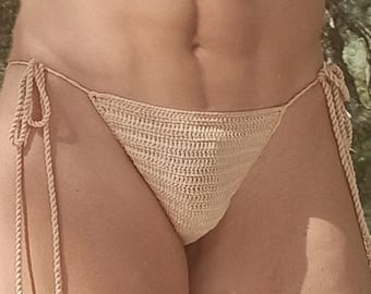 May include: A beige crochet bikini bottom with adjustable side ties. The bottoms are made of a textured, woven material and feature thick, braided ties for a secure fit. The bikini bottom is a neutral color, suitable for swimwear.