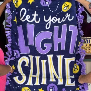 May include: Navy blue fleece blanket with the words "let your LIGHT SHINE" in white and purple. The blanket has a purple fringe border and features yellow stars and butterfly designs.