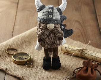 May include: A handmade crochet Viking gnome doll with a gray and white horned helmet, brown beard, and black boots. A compass, map, and leather pouch are on a burlap cloth, creating a whimsical, adventurous theme.