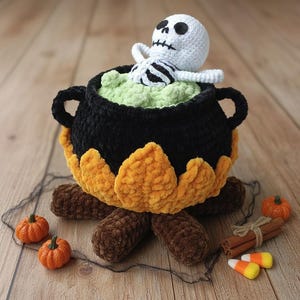 Può includere: Un calderone all'uncinetto fatto a mano a tema Halloween con una figura di scheletro bianco all'interno. Il calderone nero poggia su una base di tronchi marroni ed è circondato da zucche arancioni, bastoncini di cannella e caramelle.