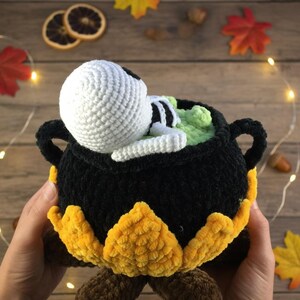 Crochet Halloween amigurumi pattern featuring a black plush cauldron with yellow flames, a bubbling green potion, and a cute white skeleton sitting inside. Perfect for spooky home décor, Halloween party centerpiece, or a handmade gift. This detailed crochet pattern is ideal for amigurumi lovers and includes step-by-step instructions. Great project for Halloween crafters looking for unique and fun holiday decorations.