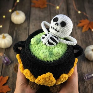 Crochet Halloween amigurumi pattern featuring a black plush cauldron with yellow flames, a bubbling green potion, and a cute white skeleton sitting inside. Perfect for spooky home décor, Halloween party centerpiece, or a handmade gift. This detailed crochet pattern is ideal for amigurumi lovers and includes step-by-step instructions. Great project for Halloween crafters looking for unique and fun holiday decorations.