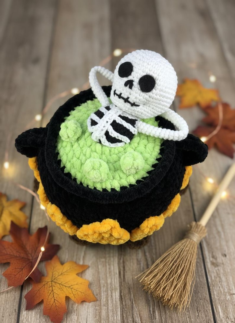 Crochet Halloween amigurumi pattern featuring a black plush cauldron with yellow flames, a bubbling green potion, and a cute white skeleton sitting inside. Perfect for spooky home décor, Halloween party centerpiece, or a handmade gift. This detailed crochet pattern is ideal for amigurumi lovers and includes step-by-step instructions. Great project for Halloween crafters looking for unique and fun holiday decorations.