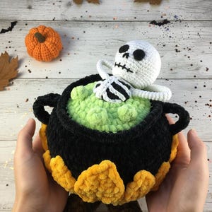 Crochet Halloween amigurumi pattern featuring a black plush cauldron with yellow flames, a bubbling green potion, and a cute white skeleton sitting inside. Perfect for spooky home décor, Halloween party centerpiece, or a handmade gift. This detailed crochet pattern is ideal for amigurumi lovers and includes step-by-step instructions. Great project for Halloween crafters looking for unique and fun holiday decorations.