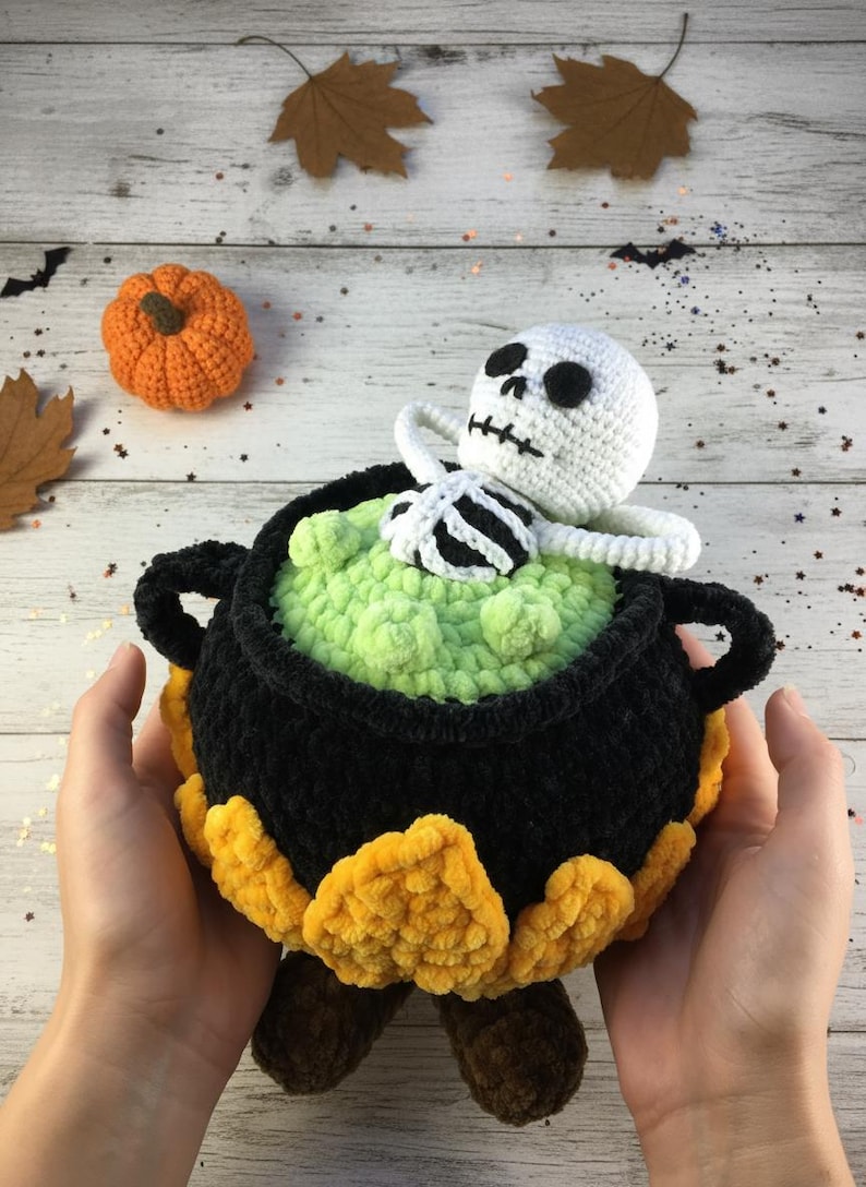 Crochet Halloween amigurumi pattern featuring a black plush cauldron with yellow flames, a bubbling green potion, and a cute white skeleton sitting inside. Perfect for spooky home décor, Halloween party centerpiece, or a handmade gift. This detailed crochet pattern is ideal for amigurumi lovers and includes step-by-step instructions. Great project for Halloween crafters looking for unique and fun holiday decorations.