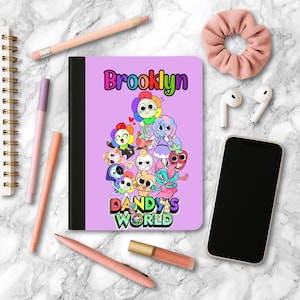 May include: A lavender notebook with the name "Brooklyn" in rainbow letters and a cartoon illustration. The notebook is surrounded by pens, a scrunchie, earbuds, a phone, and a pencil on a marble surface.