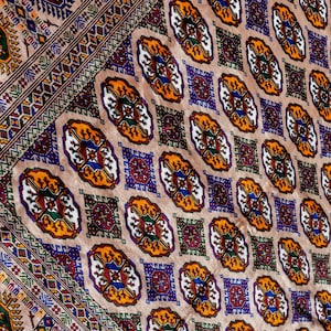 May include: A detailed rug with a beige backdrop. The design features repeating geometric shapes in red, blue, yellow, and green. The rug has a border with intricate patterns. The measurements are in centimetres.