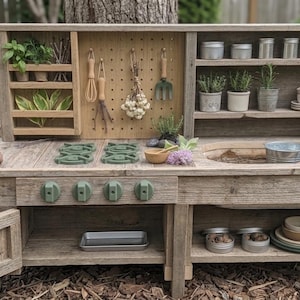 May include: A rustic wooden play kitchen with a sink, stove, and shelves. It features green knobs, a pegboard with utensils, and small potted plants. The kitchen includes a small metal sink and a variety of accessories.
