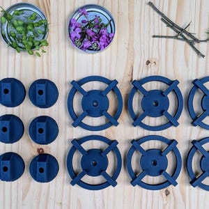 May include: An overhead shot displays an assortment of objects on a light wood surface. There are several small, dark blue, circular objects with cross-shaped designs, and other dark blue, cylindrical objects. Small jars with flowers and greenery are also present.