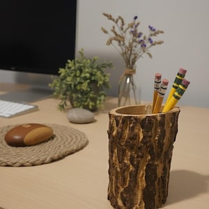 May include: A wooden pencil holder with a textured, bark-like exterior. The holder contains several yellow pencils with pink erasers. The desk also features a computer monitor, a small plant, and a decorative mouse pad.