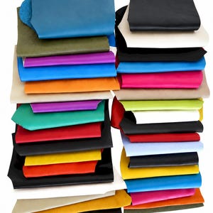 Könnte beinhalten: Eine Sammlung gestapelter Lederstücke in einer Vielzahl lebendiger Farben, darunter Blau, Schwarz, Olivgrün, Violett, Orange, Rot, Gelb, Weiß und Pink. Die rechteckigen Stücke sind in zwei Spalten geschichtet und zeigen glatte Texturen.