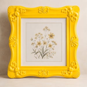 Puede incluir: Una pieza de arte mural cuadrada que presenta una ilustración botánica de flores silvestres en tonos beige y verde, encerrada en un marco amarillo brillante con detalles decorativos moldeados en forma de concha en los lados.
